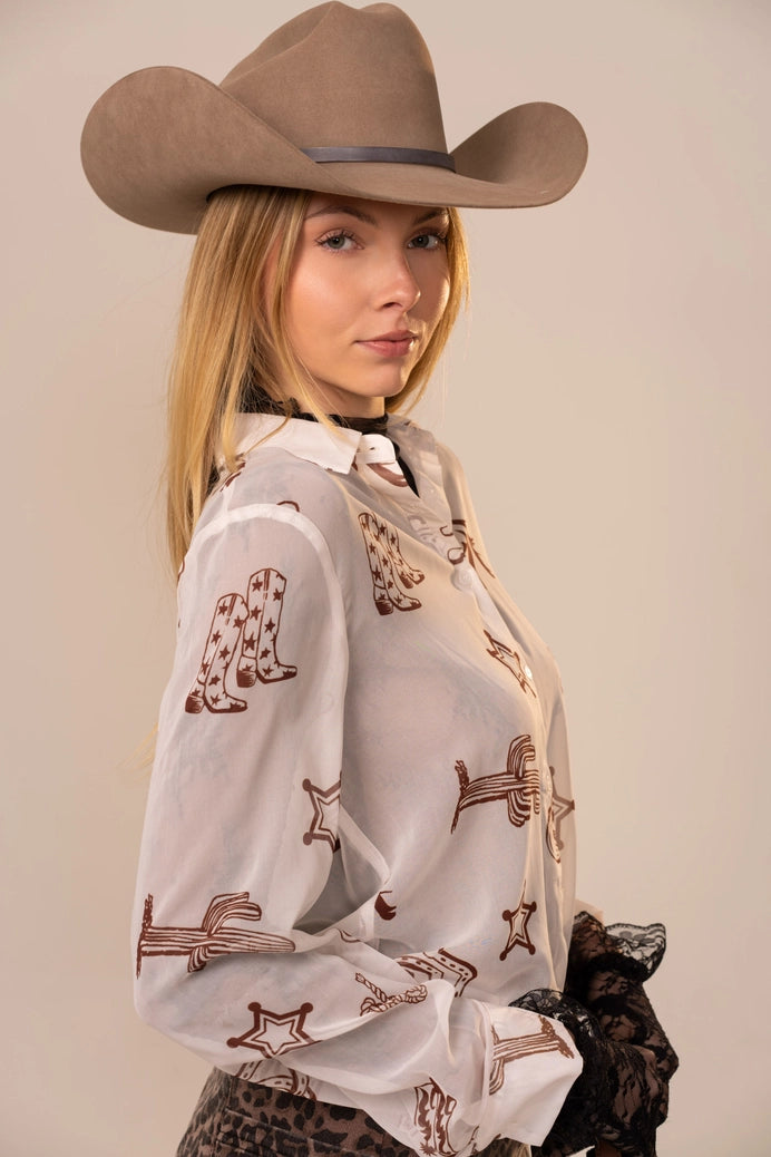 Woman wearing a cowboy hat and a white blouse with brown patterns on a plain background