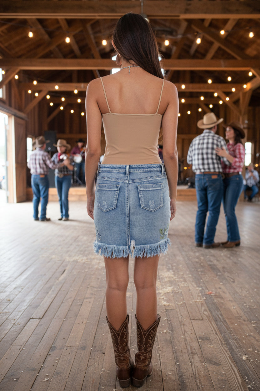 Woman wearing a beige top and denim skirt with cowboy boots