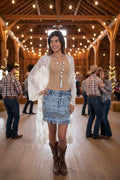 Woman wearing a beige top, denim skirt, and lace cardigan on a white background