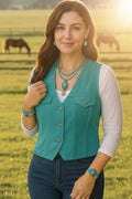 Woman wearing a teal vest and jewelry in a field with horses in the background