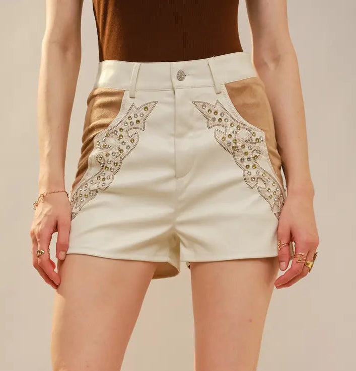 Person wearing brown knee-high boots, white shorts with lace trim, and a brown top on a neutral background.
