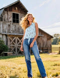 Woman Wearing a mint colored sleeveless shirt  standing in a field with a wooden barn in the background